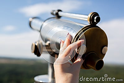 Female hand adjusts sharpness on a touristic telescope against forest panorama Stock Photo