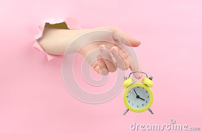 A female hand through the background holds a yellow retro alarm clock. At 15.55 hours, the concept of a seven-hour working day. Stock Photo