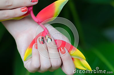 Female hand with color nail art stickers holding Heliconia plant Stock Photo