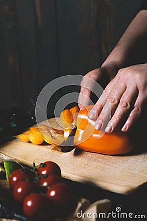 Female hand in cooking process sweet pepper on cutting board on a black background of the old wooden boards vintage top view Stock Photo