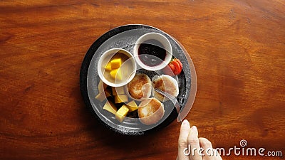 A female hand cutting a coconut fritter pastry with a fork. A delicious photo of tropical breakfast with pastries Stock Photo