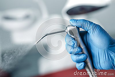 Female hand of dentist in blue gloves holding air water syringe, blurred background of clinic with dental unit, dentistry and Stock Photo