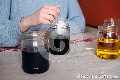 Female hand dying easter egg on blue liquid. Stock Photo