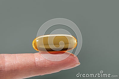 Female hand holding a big yellow capsule of nutritional supplement. Food supplement, vitamin D, omega, vitamin C. Stock Photo
