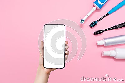 Female hand holding cellphone and various toothbrushes, toothpaste and mouth freshener, on a pink background. Mock up. The concept Stock Photo