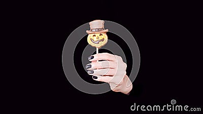 Female hand holding chocolate candy little pumpkin on the stick, black panorama background. Copy space Stock Photo