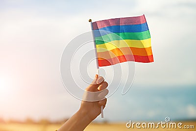 Female hand holding colorful rainbow lgbt flag against blue sky Stock Photo