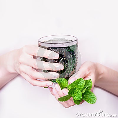 Female hand holding glass of green chlorophyll drink with mint leaves on a light pink background Stock Photo
