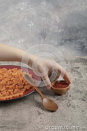 Female hand holding ground pepper and burgundy plate macaroni Stock Photo