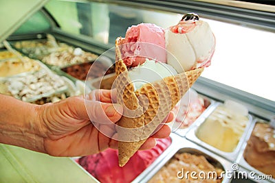 Female hand is holding a large strawberry, mint, vanilla with sour cherry ice cream in waffle cone. Stock Photo