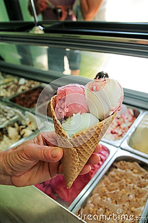Female hand is holding a large strawberry, mint, vanilla with sour cherry ice cream in waffle cone. Stock Photo