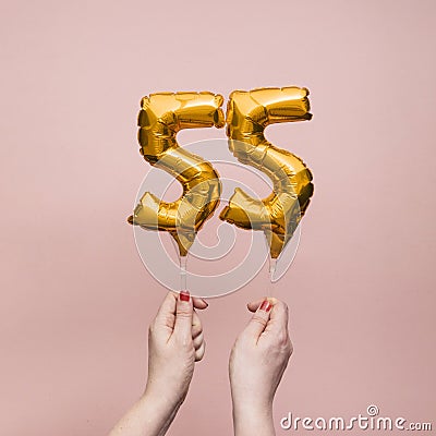 Female hand holding a number 55 birthday anniversary celebration gold balloon Stock Photo