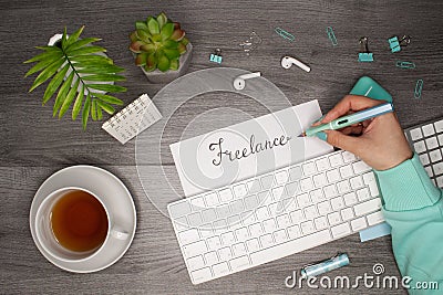 Female hand holding a pen and writing `freelance` in notepad. Business flat layout Stock Photo