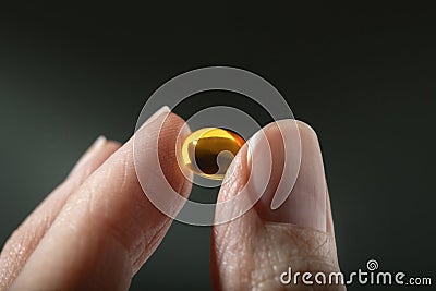 Female hand holding a small yellow capsule of nutritional supplement. Food supplement, vitamin D, omega, vitamin C. Stock Photo