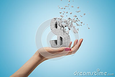 Female hand holding stone concrete dollar sign shattering into pieces on blue background Stock Photo