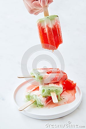 Ice cream lolly in a plate with splashes. A woman`s hand holds a melting ice cream on a white marble background with Stock Photo