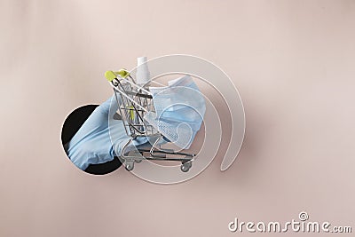 Female hand holds grocery trolley in protective mask and antiseptic for hands through a round hole in pink paper, Concept of Stock Photo