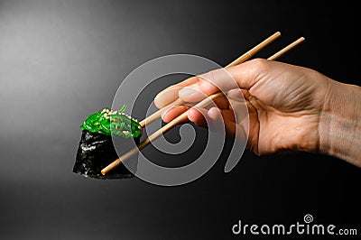 Female hand holds roll of gunkan sushi with chukka and sesame seeds wrapped in nori seaweed with chopsticks on dark Stock Photo