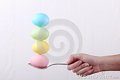 Female hand holds a spoon on which multi-colored eggs are balanced, on a white background. Unusual design, Easter concept, copy Stock Photo