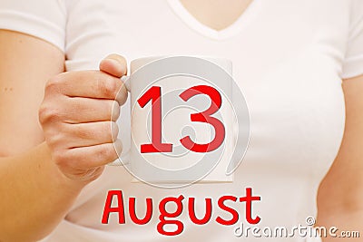 A female hand holds a white mug with the inscription 13 August. Business and holiday concept Stock Photo