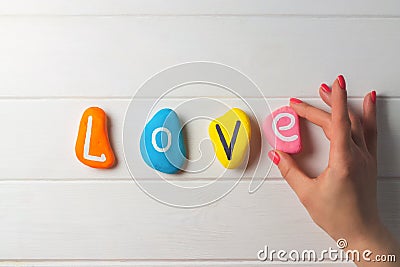 Female hand laying out text Love written on colored pebbles on white wooden surface. Flat lay. Copy space Stock Photo