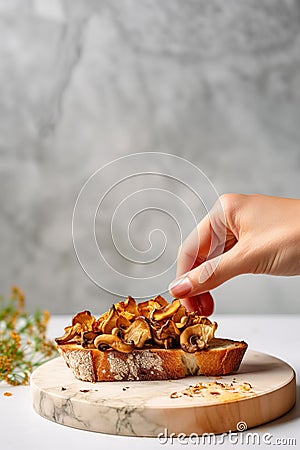 Female hand making a toast with roasted chanterelles, on marble countertop. Fried wild mushrooms. Generative AI Stock Photo