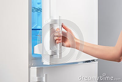 Female hand opening white refrigerator door on gray Stock Photo