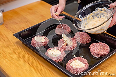 Female hand overlays stuffing theminced meat or meatballs laying on a black baking tray. Process of cooking Stock Photo