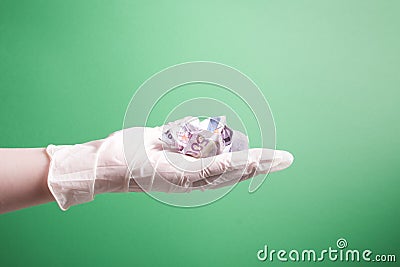 female hand in a rubber white medical disposable glove holds a crumpled 500 euro bill green background Stock Photo