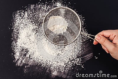 Female hand sifts flour on a black background Stock Photo