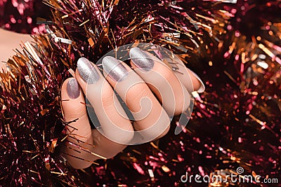 Female hand with silver Christmas nail design. Silver nail polish manicure. Female hand holding orange New Year tinsel Stock Photo