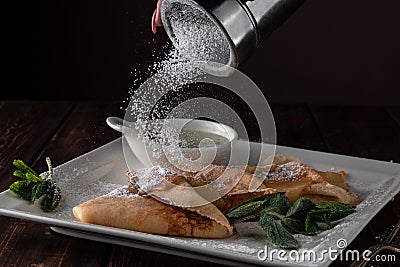 Female hand sprinkling icing sugar on pancakes stuffed with pear and cheese, wooden table served in restaurant in rustic style, Stock Photo