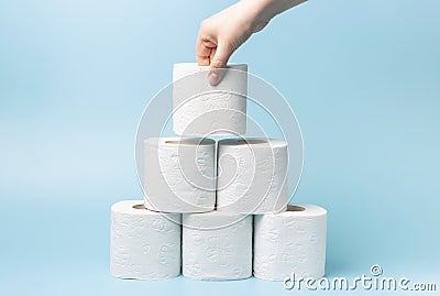 Female hand stacks toilet paper in a stack on blue background close-up Stock Photo