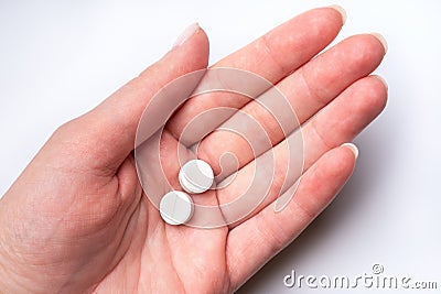 Female hand on white background holds two white pills. Dose of medicines Stock Photo