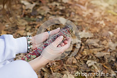 Female hands with bracelets hold a herbal fumigation twist when meditating outdoors. A bunch of field herbs for Stock Photo