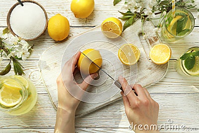 Female hands cuts lemon for making lemonade on white wooden background Stock Photo