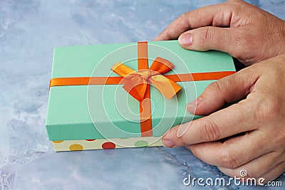 Female hands giving a wrapped Christmas or other holiday handmade gift with orange ribbon Stock Photo