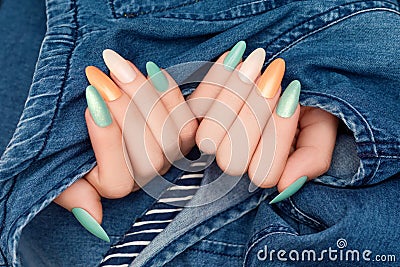 Female hands with glitter nail polish. Green and orange nail design with two shades. Women hand with sparkle manicure on blue Stock Photo