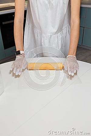 Female hands in gloves roll out mastic with rolling pin to make decor for cupcakes, white table background Stock Photo