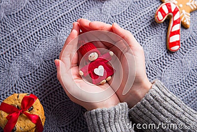 Female hands in gray knitted sweater holding little doll on Christmas decorative background Stock Photo