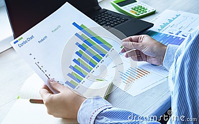 Female hands hold documents and business graphics on the background of a laptop. The girl works in the home office at the table Stock Photo