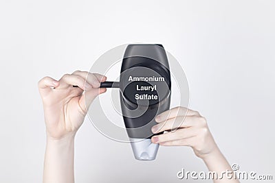 Chemical components on the shampoo label: Ammonium Lauryl Sulfate. Female hands hold a magnifying glass on the jar, which Stock Photo