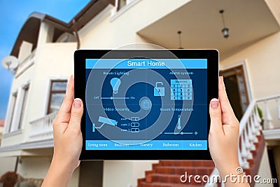 Female hands hold a tablet with system smart house on the background of the house Stock Photo