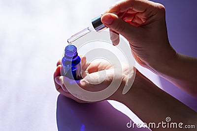 Female hands is holding blue glass bottle and pipette full of cosmetic serum for skin care treatment. Stock Photo