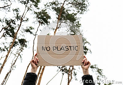 Female hands holding cardboard with text NO PLASTIC outdoors. Nature background. Protester activist Stock Photo