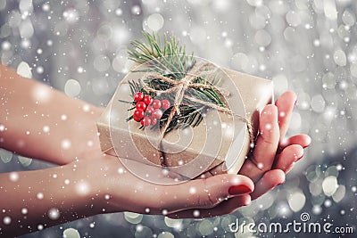 Female hands holding Christmas gift box with branch of fir tree, shiny xmas background. Holiday gift and decoration Stock Photo