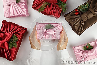 Female hands holding a gift. Japanese wrapping cloth Furoshiki. Silk pink cloth with green fir and pine cones. Stock Photo