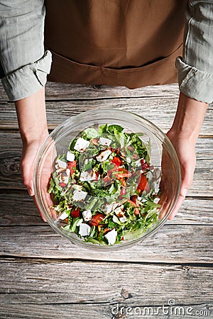 Female hands holding a glass bowl of vegetable salad with feta over a wooden background Stock Photo