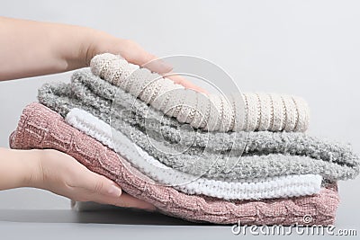 female hands holding a pile pastel color jumpers and other knitted clothing. winter apparel, trendy pale textured Stock Photo