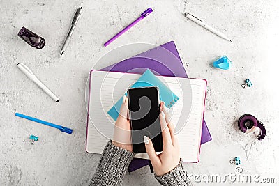 Female hands holding smartphone at workplace with notepads, pens and other office supplies. Women`s business concept Stock Photo